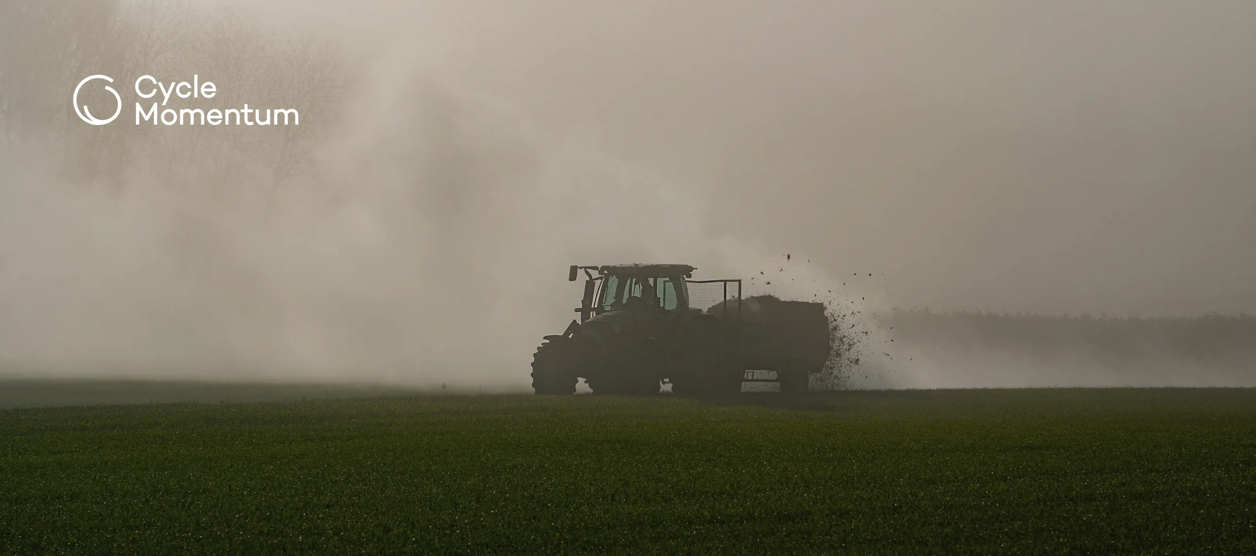 Tractor spreading manure across a field on a misty autumn morning